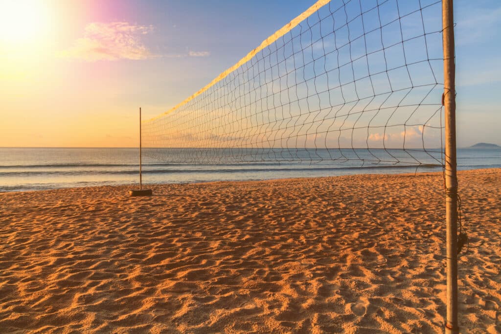 Volleyball net stretched on two posts over a sandy beach at sunrise, with the sea in the background