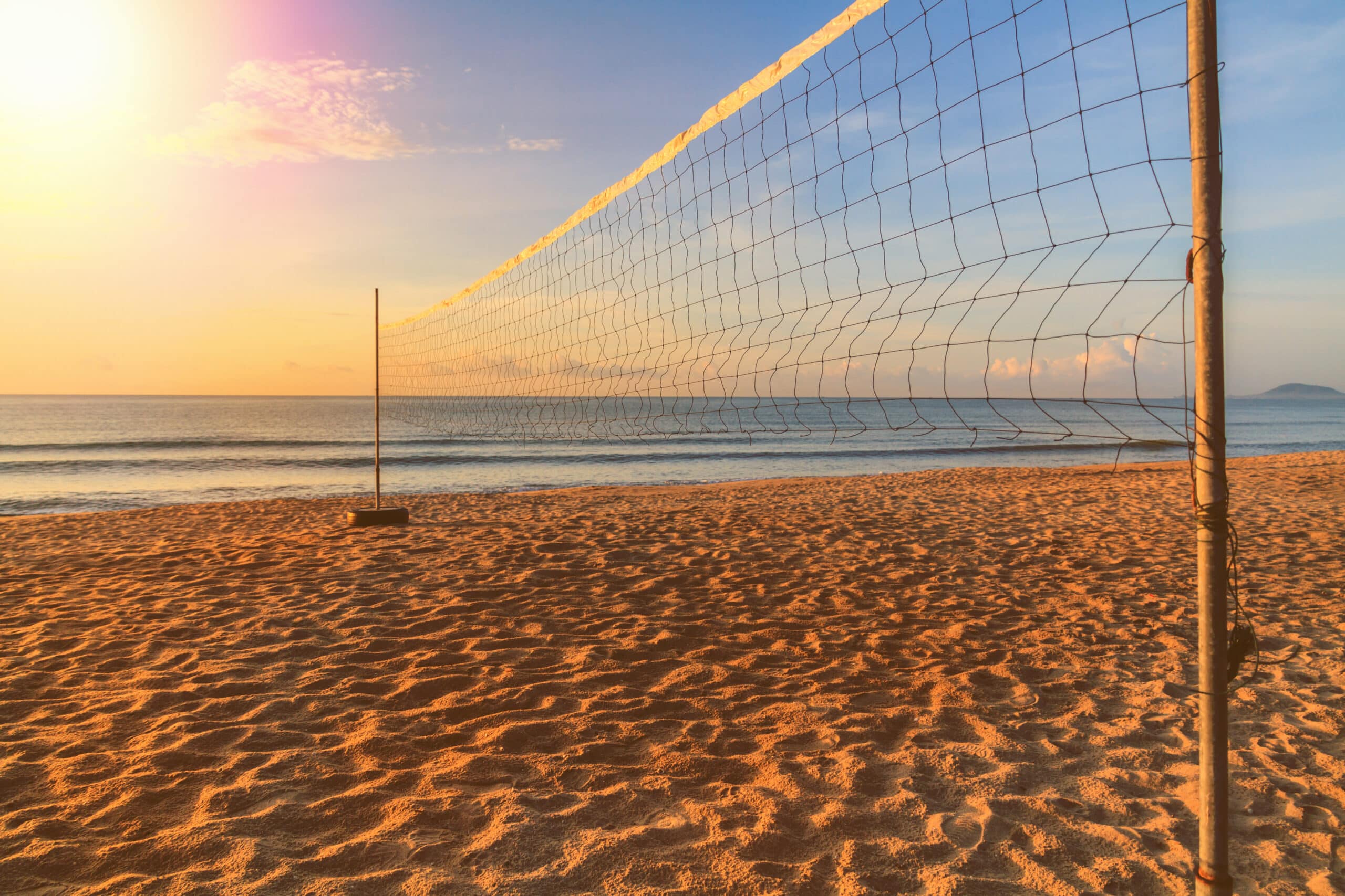 Volleyball net stretched on two posts over a sandy beach at sunrise, with the sea in the background
