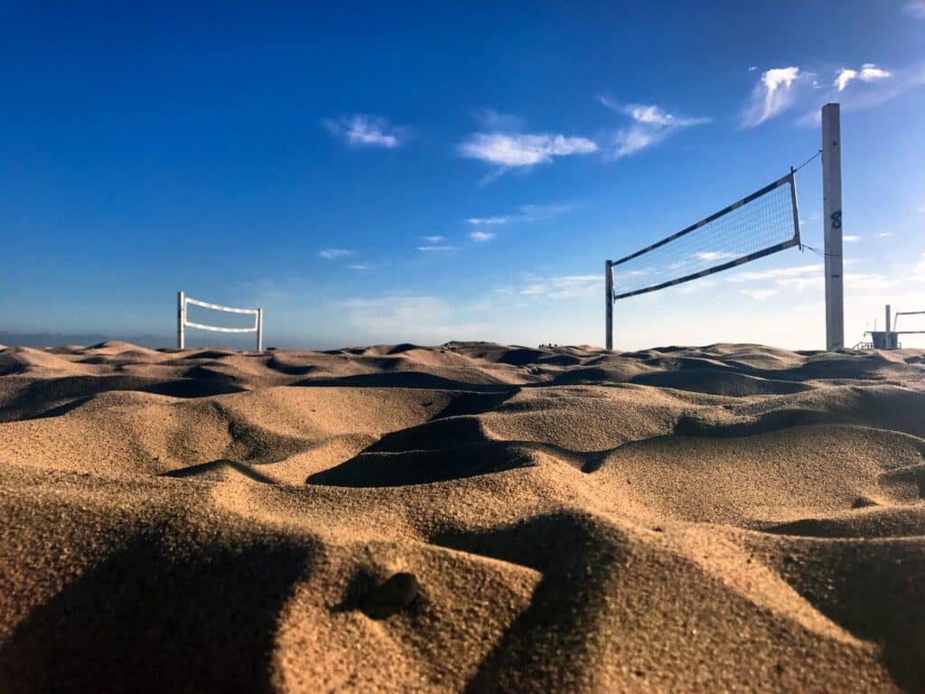 Beach volleyball net standing in windswept sand dunes under a clear blue sky, with a second net visible in the distance