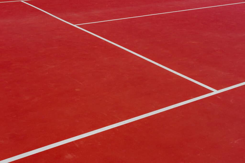 Close-up corner of a red tennis court where two painted white lines cross at a right angle