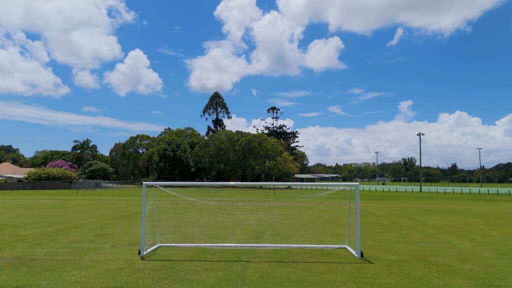 Empty portable soccer goal on an open grass field under a partly cloudy sky