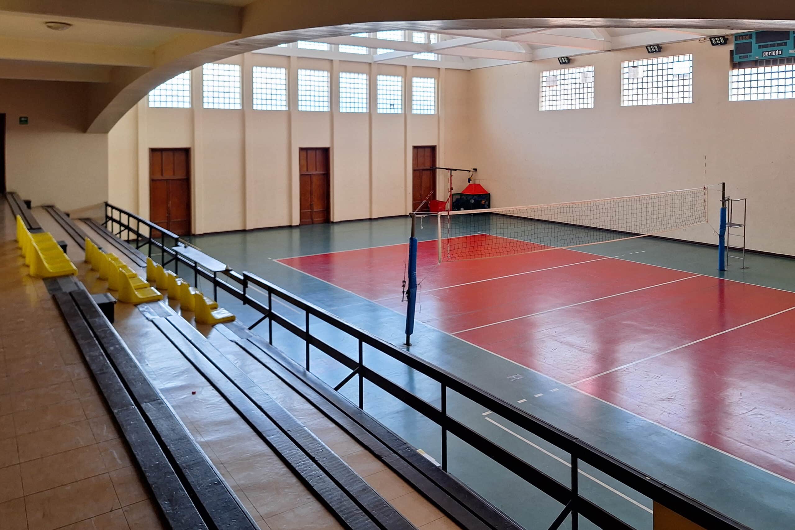 Empty indoor volleyball court with a red and green surface, boundary lines, and a net strung between two posts