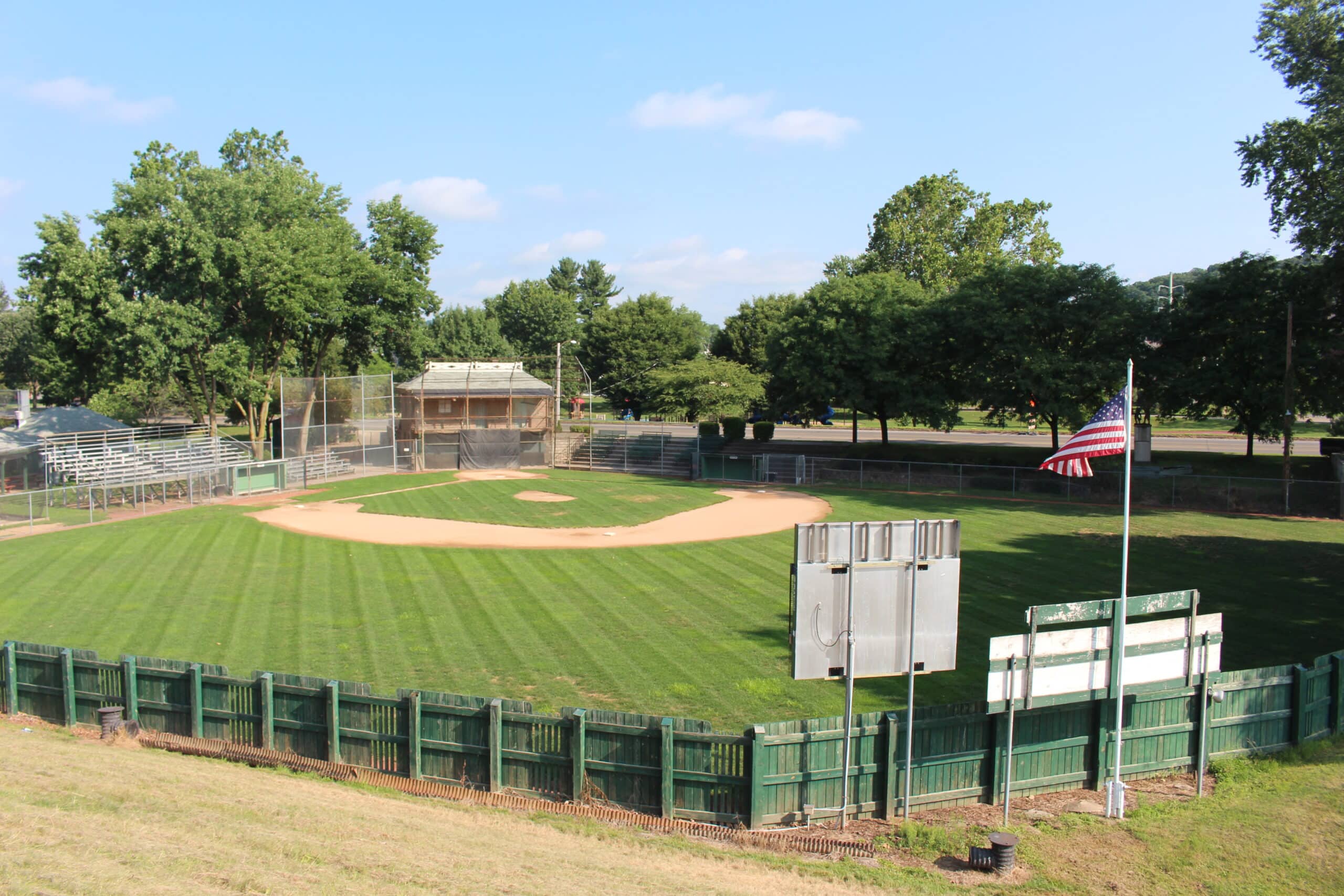 Small empty baseball diamond with a sand infield, mown outfield grass, and a low wooden outfield fence